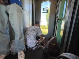 満席の列車の通路に座り込み、疲れ果てた様子で移動するバックパッカーたち